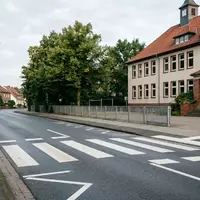 Ein leerer Fußgängerüberweg vor einem Schulgebäude am frühen Morgen bei Tageslicht. - Foto: über boerse-global.de