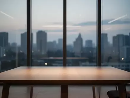 Ein minimalistischer, moderner Büroraum mit einem leeren Holztisch vor einer großen Fensterfront in der Dämmerung. - Foto: über boerse-global.de