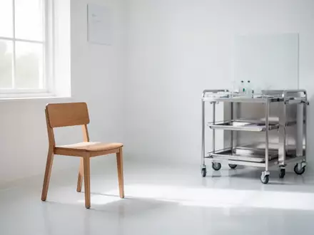Ein minimalistischer Behandlungsraum in einer Arztpraxis mit einem leeren Stuhl und einem medizinischen Rollwagen. - Foto: ĂĽber boerse-global.de