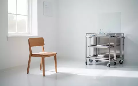 Ein minimalistischer Behandlungsraum in einer Arztpraxis mit einem leeren Stuhl und einem medizinischen Rollwagen. - Foto: über boerse-global.de
