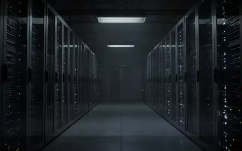 Dunkler, industrieller Serverraum mit metallischen Rack-Reihen in kühlem, atmosphärischem Licht. - Foto: über boerse-global.de