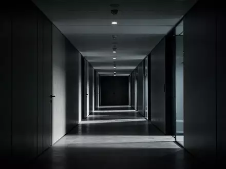 Ein minimalistischer, dunkel beleuchteter moderner Büroflur mit langen Schatten und architektonischen Linien. - Foto: über boerse-global.de