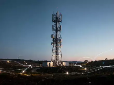 Ein moderner Mobilfunkmast bei Dämmerung in einer weitläufigen Landschaft als Symbol für globale Netzwerkkonnektivität. - Foto: über boerse-global.de