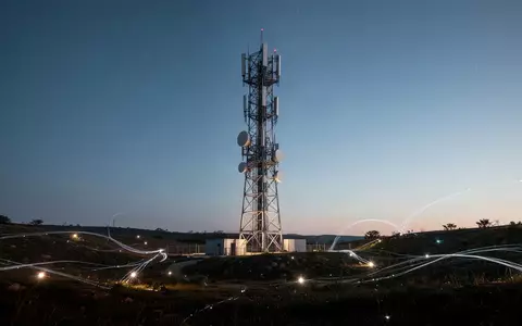 Ein moderner Mobilfunkmast bei Dämmerung in einer weitläufigen Landschaft als Symbol für globale Netzwerkkonnektivität. - Foto: über boerse-global.de