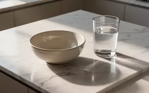Ein minimalistisch gestalteter Küchentisch mit einer leeren Schale und einem Glas Wasser in hellem, natürlichem Licht. - Foto: über boerse-global.de