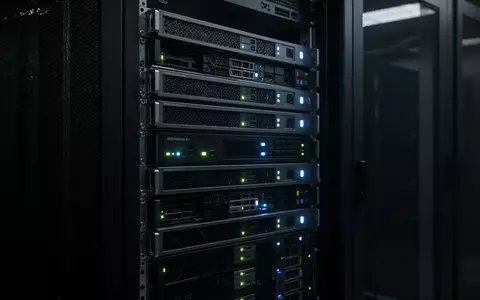 Ein dunkler Serverraum mit leuchtenden Status-LEDs an Hardware-Racks, die eine technische und industrielle Umgebung darstellen. - Foto: über boerse-global.de