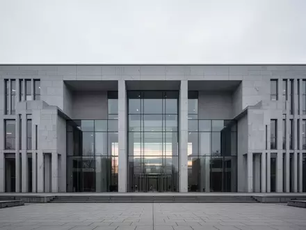 Moderne, minimalistische Architektur eines öffentlichen Gebäudes mit grauer Steinfassade und Glasfront unter bewölktem Himmel. - Foto: über boerse-global.de