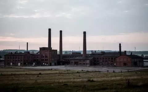 Eine weitläufige, menschenleere Industrielandschaft mit alten Fabrikgebäuden und Schornsteinen vor einem bewölkten Himmel. - Foto: über boerse-global.de