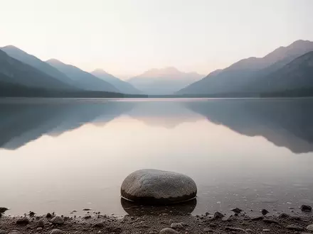 Ein ruhiger Bergsee bei Tagesanbruch spiegelt den Himmel wider, mit einem einzelnen Stein am Ufer, der Stille und Reflexion symbolisiert. - Foto: über boerse-global.de