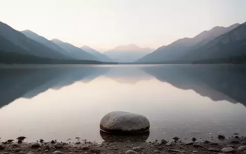 Ein ruhiger Bergsee bei Tagesanbruch spiegelt den Himmel wider, mit einem einzelnen Stein am Ufer, der Stille und Reflexion symbolisiert. - Foto: ĂĽber boerse-global.de