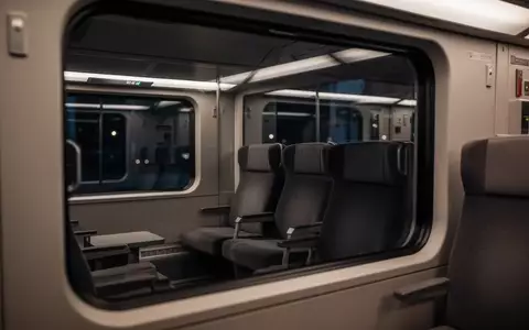 Ein menschenleeres Zugabteil bei Nacht mit gedimmter Beleuchtung und Blick durch ein Fenster. - Foto: über boerse-global.de