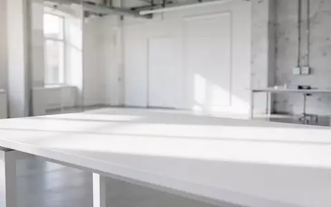 Ein minimalistischer, heller Arbeitsplatz mit einer leeren weißen Schreibtischoberfläche und dezenter, moderner Architektur im Hintergrund. - Foto: über boerse-global.de