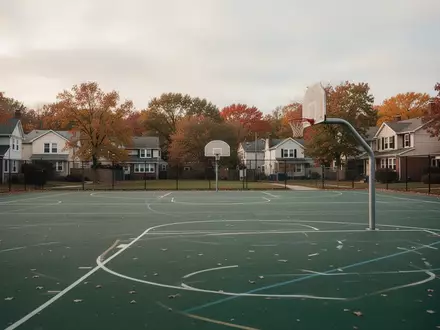 Ein leerer Sportplatz einer Grundschule in einem Wohngebiet mit einem Basketballkorb an einem bewölkten Tag. - Foto: über boerse-global.de