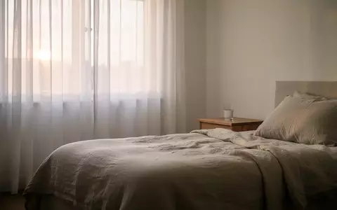 Ein minimalistisch eingerichtetes Schlafzimmer in der Morgendämmerung mit weichem Lichteinfall durch helle Vorhänge. - Foto: über boerse-global.de