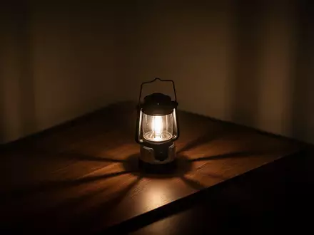 Ein abgedunkelter Raum, der in der Dämmerung nur von einer einzelnen, hell leuchtenden Laterne auf einem Holztisch erhellt wird. - Foto: über boerse-global.de