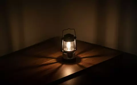 Ein abgedunkelter Raum, der in der Dämmerung nur von einer einzelnen, hell leuchtenden Laterne auf einem Holztisch erhellt wird. - Foto: über boerse-global.de