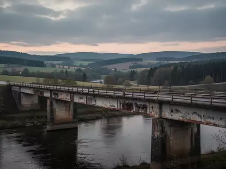 Eine marode Autobahnbrücke über einem Flusstal in einer bewaldeten Landschaft bei bewölktem Himmel. - Foto: über boerse-global.de