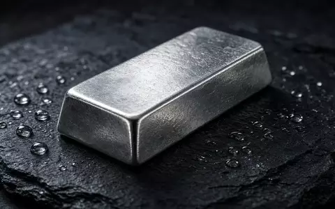 Ein einzelner Silberbarren auf einer dunklen, reflektierenden Schieferplatte mit Öltropfen in stimmungsvollem Licht. - Foto: über boerse-global.de