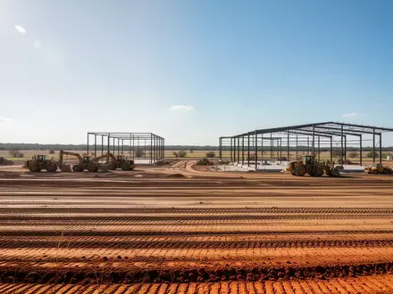 Eine weite Baustelle mit planiertem Boden und Stahlkonstruktionen in der texanischen Landschaft unter blauem Himmel. - Foto: über boerse-global.de