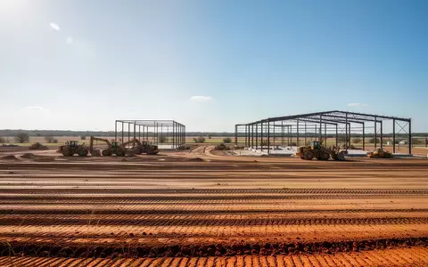 Eine weite Baustelle mit planiertem Boden und Stahlkonstruktionen in der texanischen Landschaft unter blauem Himmel. - Foto: über boerse-global.de