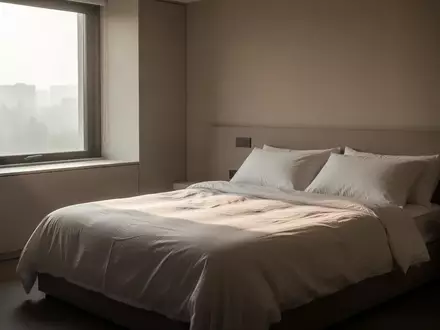 Ein minimalistisch eingerichtetes Schlafzimmer bei Tagesanbruch mit sanftem Lichteinfall auf ein unbenutztes, ordentlich gemachtes Bett. - Foto: über boerse-global.de