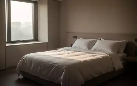 Ein minimalistisch eingerichtetes Schlafzimmer bei Tagesanbruch mit sanftem Lichteinfall auf ein unbenutztes, ordentlich gemachtes Bett. - Foto: ĂŒber boerse-global.de