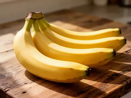 Mehrere frische, noch leicht grünliche Bananen liegen auf einer hölzernen Arbeitsfläche in natürlichem Tageslicht. - Foto: über boerse-global.de