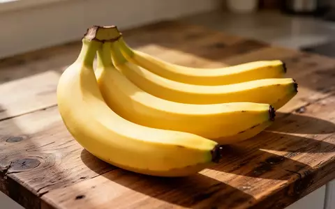 Mehrere frische, noch leicht grünliche Bananen liegen auf einer hölzernen Arbeitsfläche in natürlichem Tageslicht. - Foto: über boerse-global.de