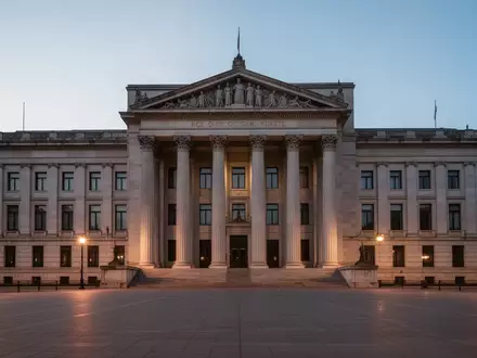 Ein imposantes, steinernes Gerichtsgebäude in der Abenddämmerung mit einem leeren Platz im Vordergrund. - Foto: über boerse-global.de