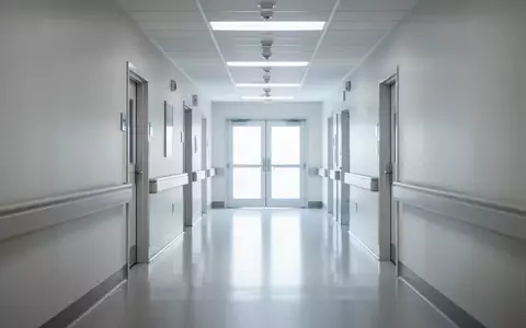 Ein heller, menschenleerer Krankenhausflur in einer modernen Klinik mit reflektierendem Boden und einer Tür am Ende. - Foto: über boerse-global.de