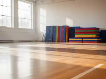 Eine helle, leere Sporthalle mit poliertem Holzboden und ordentlich gestapelten Gymnastikmatten im Hintergrund. - Foto: über boerse-global.de