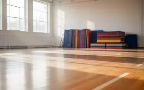 Eine helle, leere Sporthalle mit poliertem Holzboden und ordentlich gestapelten Gymnastikmatten im Hintergrund. - Foto: über boerse-global.de