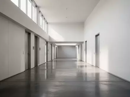Ein leerer, minimalistischer Flur in einer Behörde mit polierten Betonböden und weißen Wänden bei natürlichem Tageslicht. - Foto: über boerse-global.de