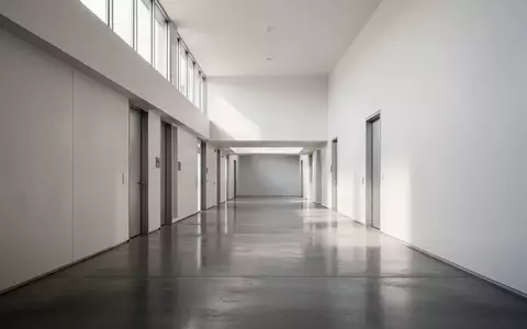 Ein leerer, minimalistischer Flur in einer Behörde mit polierten Betonböden und weißen Wänden bei natürlichem Tageslicht. - Foto: über boerse-global.de