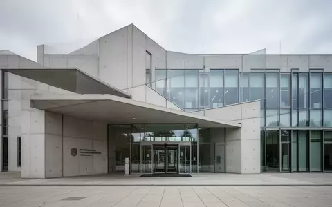 Modernes Verwaltungsgebäude mit einer klaren, minimalistischen Fassade aus Glas und Sichtbeton bei Tageslicht. - Foto: über boerse-global.de