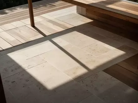 Sonnige Terrasse mit geometrischem Schattenwurf auf einem Steinboden ohne Möbel. - Foto: über boerse-global.de