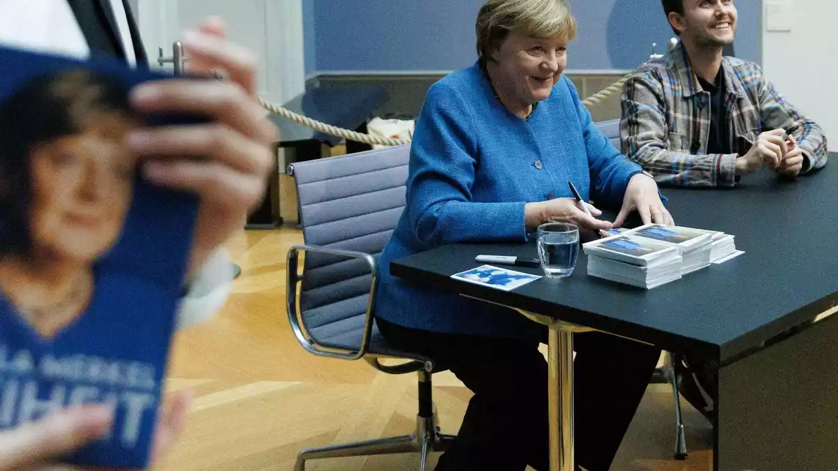 Merkel signiert Kunstpostkarten im Bode-Museum neben dem Maler ihres dort ausgestellten Porträts, Jérémie Queyras.  - Bild: Carsten Koall/dpa