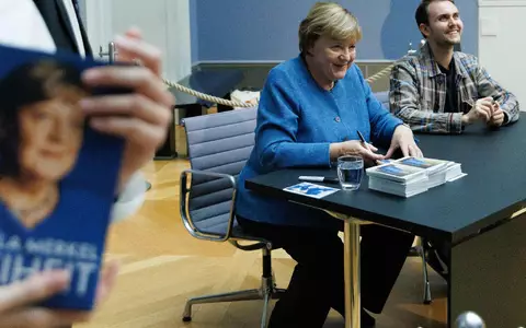 Merkel signiert Kunstpostkarten im Bode-Museum neben dem Maler ihres dort ausgestellten Porträts, Jérémie Queyras.  - Foto: Carsten Koall/dpa