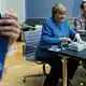 Merkel signiert Kunstpostkarten im Bode-Museum neben dem Maler ihres dort ausgestellten Porträts, Jérémie Queyras.  - Bild: Carsten Koall/dpa