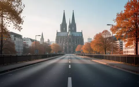Eine leere Asphaltstraße in Köln mit dem Kölner Dom im unscharfen Hintergrund an einem sonnigen Herbsttag. - Foto: über boerse-global.de