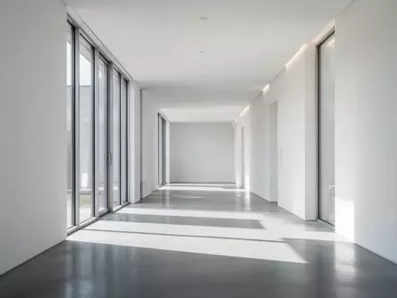Ein minimalistischer, heller Flur mit klaren Linien und geometrischem Schattenwurf in einem modernen Gebäude. - Foto: über boerse-global.de