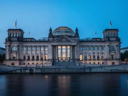 Das Berliner Reichstagsgebäude in der Dämmerung, aufgenommen aus der Ferne über die Spree. - Foto: über boerse-global.de