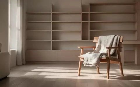Ein minimalistisch eingerichteter, lichtdurchfluteter Wohnraum mit aufgeräumten Regalen und einer schlichten Textilie auf einem Holzstuhl. - Foto: über boerse-global.de