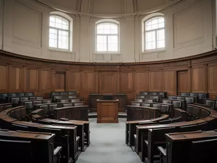 Leerer Plenarsaal mit hölzernen Sitzreihen in einem historischen Parlamentsgebäude bei natürlichem Tageslicht. - Foto: über boerse-global.de