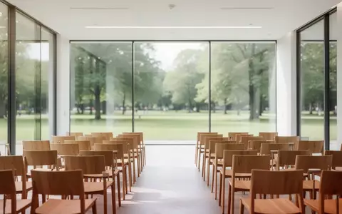 Ein heller, minimalistischer Seminarraum mit leeren Stühlen und großen Fenstern, die den Blick ins Grüne freigeben. - Foto: über boerse-global.de
