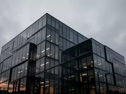 Moderne Glasfassade eines Bürogebäudes in der Abenddämmerung unter einem bewölkten Himmel. - Foto: über boerse-global.de