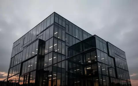 Moderne Glasfassade eines Bürogebäudes in der Abenddämmerung unter einem bewölkten Himmel. - Foto: über boerse-global.de