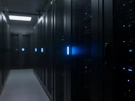 Dunkler Serverraum mit bläulich leuchtenden Status-LEDs an metallischen Gehäusen. - Foto: über boerse-global.de