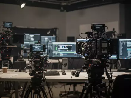 Ein professioneller, leicht abgedunkelter Arbeitsplatz in einem Fernsehstudio mit Kameratechnik im Hintergrund. - Foto: über boerse-global.de