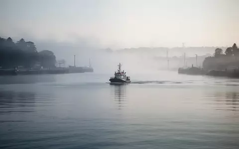 Ein ruhiges Hafenbecken im morgendlichen Nebel mit einem in der Ferne fahrenden Lotsenboot. - Foto: über boerse-global.de